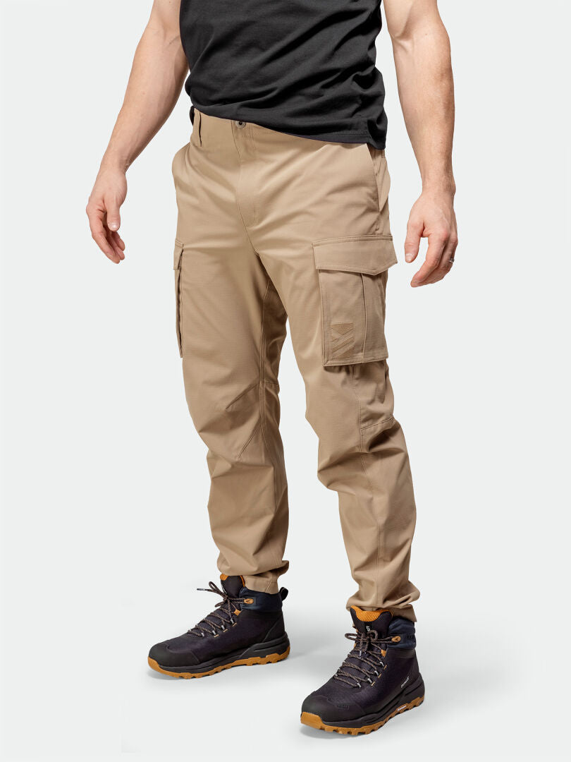 A person in Halti Roams Cargo Pants, a black t-shirt, and hiking boots stands against a plain light background.