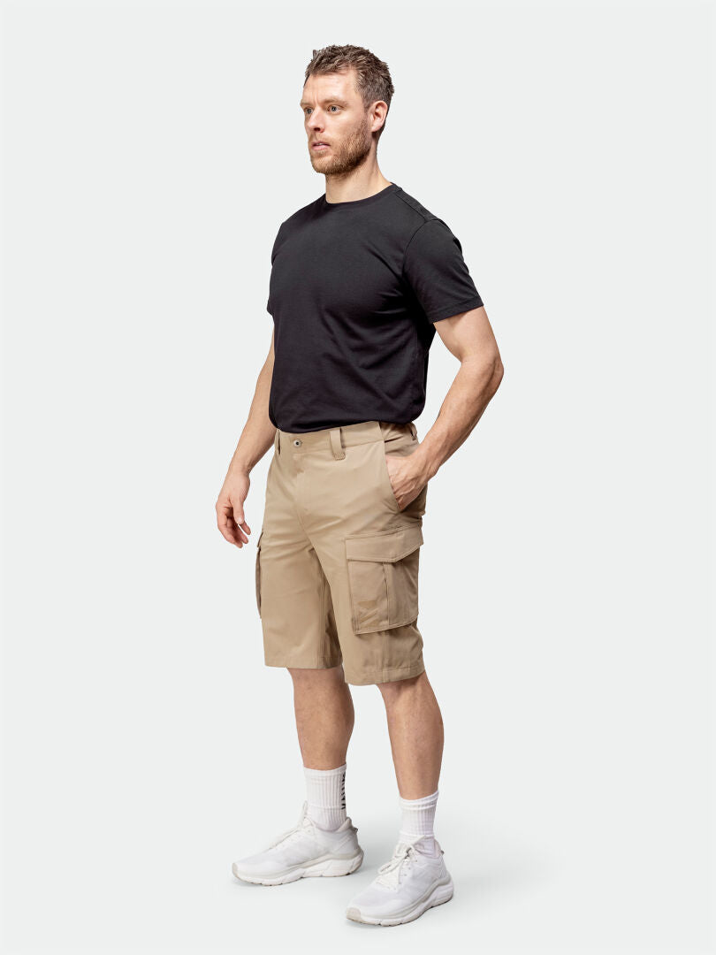 A man wears Halti Roams Shorts Mens in beige ripstop, a black t-shirt, and white sneakers against a plain background.