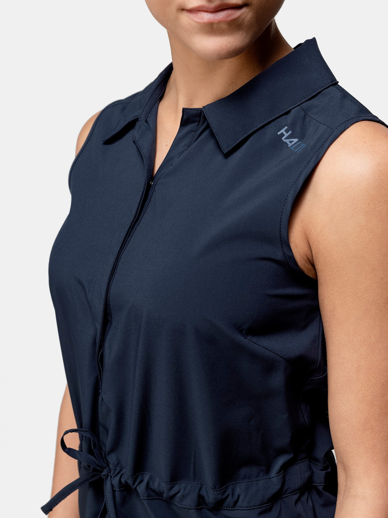 A woman wears the Halti Chipper X-stretch Dress: sleeveless, navy, collared, waist tie, quick-dry, H4H logo.