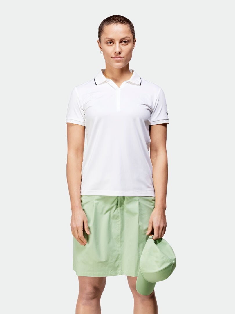 Woman in Halti Drive X-stretch Skort and white polo holds a matching cap, ready for outdoor activities.