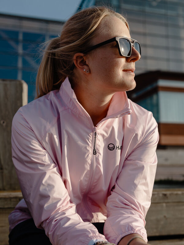 A woman in the Halti Saime Windbreaker Jacket sits outdoors on a sunny day, gazing into the distance.