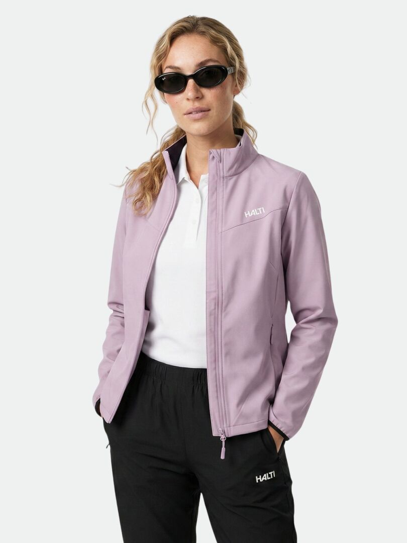 A woman in the Halti Wedge Softshell Jacket, white shirt, black pants, and sunglasses stands against a plain background.
