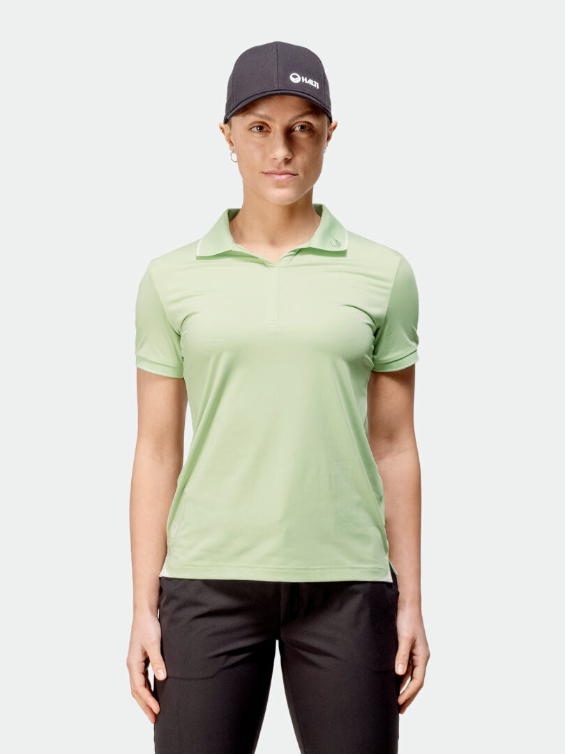A person wears a Halti Swingi Technical Polo Womens (light green), black pants, and a dark gray cap.