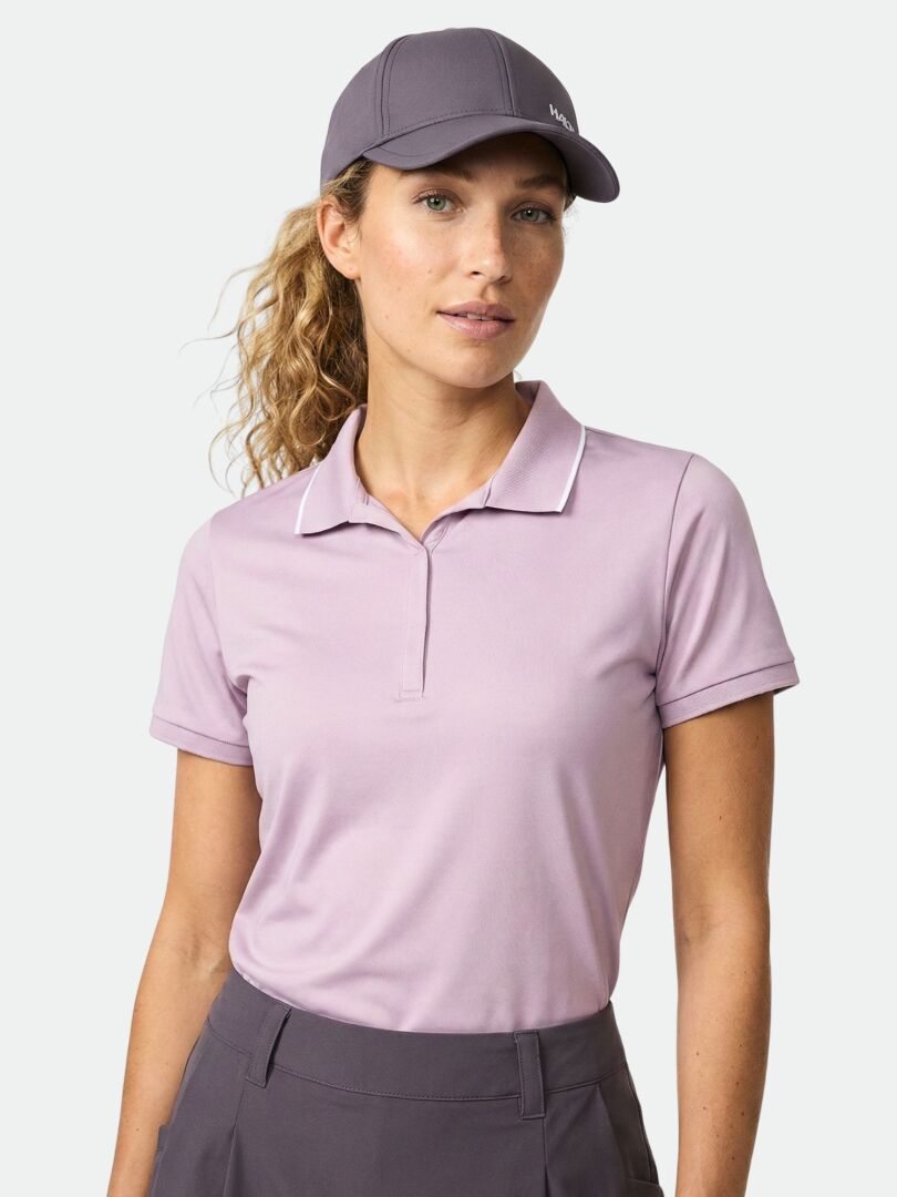 Woman in a Halti Swingi Technical Polo Shirt (lavender) and gray cap stands against a plain light background.