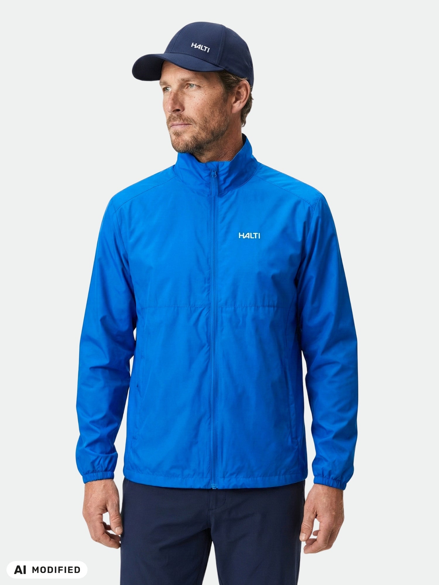 Man in Halti Saime Windbreaker Jacket and cap, made from recycled materials, stands against a plain white background.