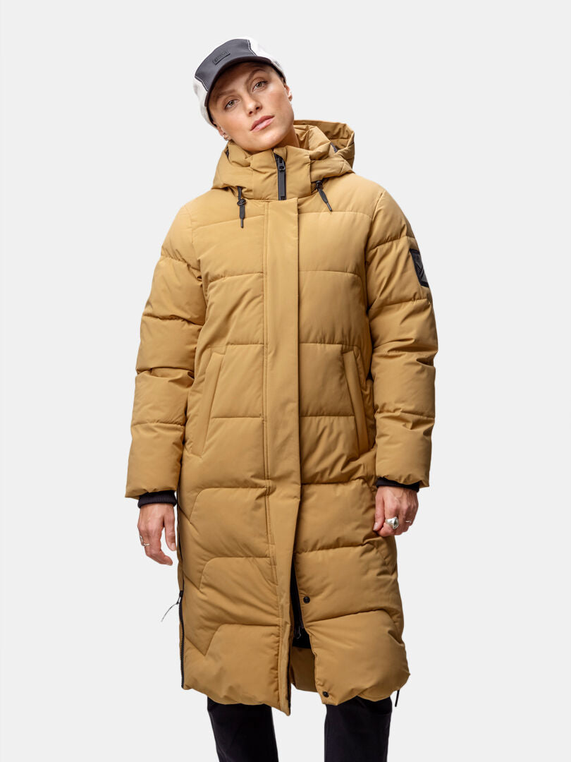 Woman in Halti Brahe Puffer Long Winter Jacket and black-and-white cap, standing against a plain background.