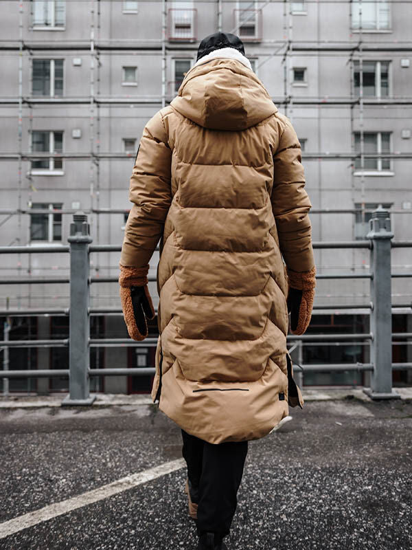 Woman in Halti's Brahe Puffer Long Winter Jacket walks past a grey city building on a winter day.