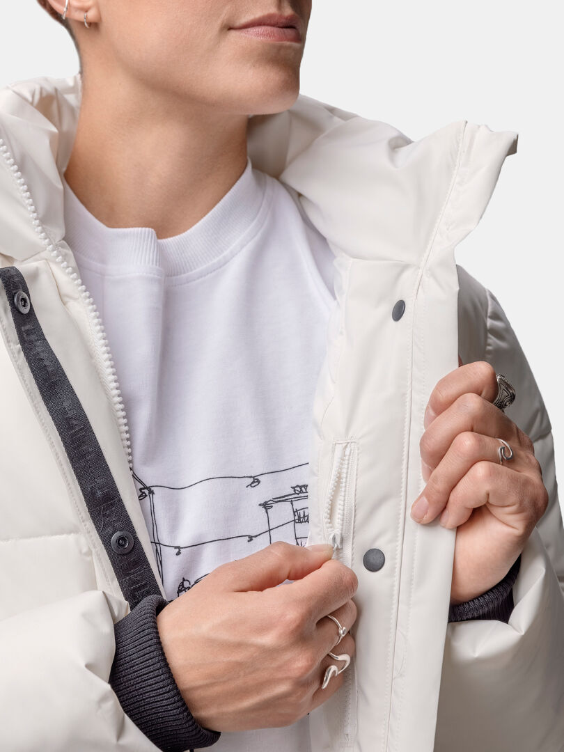 A woman adjusts the zipper on a Halti Brahe Puffer Winter Jacket made from recycled polyester, holding the collar.
