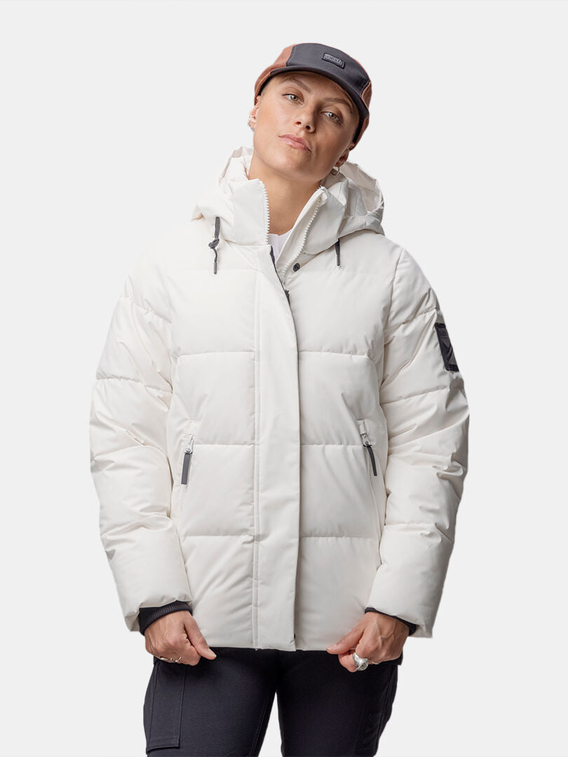 A person wears the Halti Brahe Puffer Winter Jacket Women's with black pants and a brown cap against a white background.