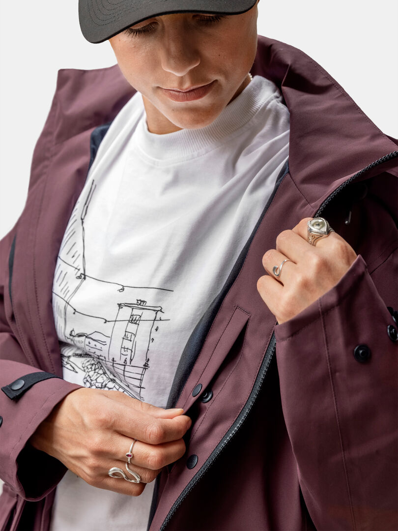 Person unzipping a maroon Halti Tokoi II DX Parka Jacket over a white graphic tee, rings on their fingers.