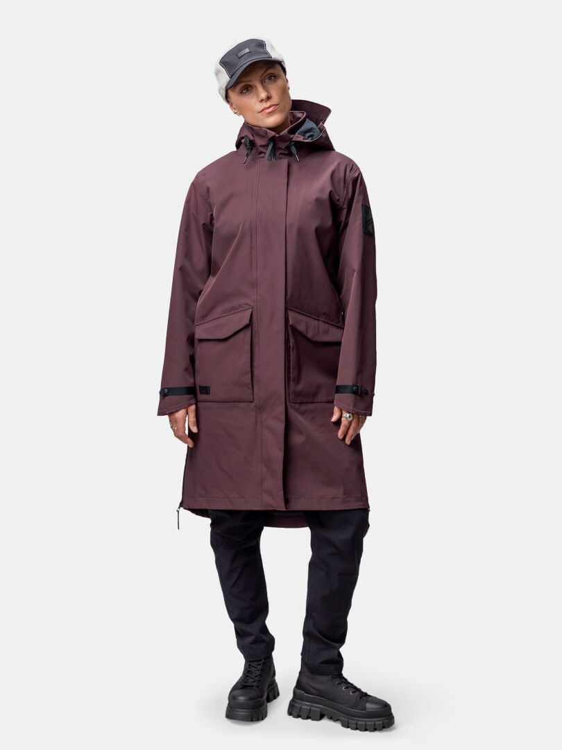 A person wears a maroon Halti Tokoi II DX Parka Jacket, black pants, chunky black boots, and a gray cap facing forward.