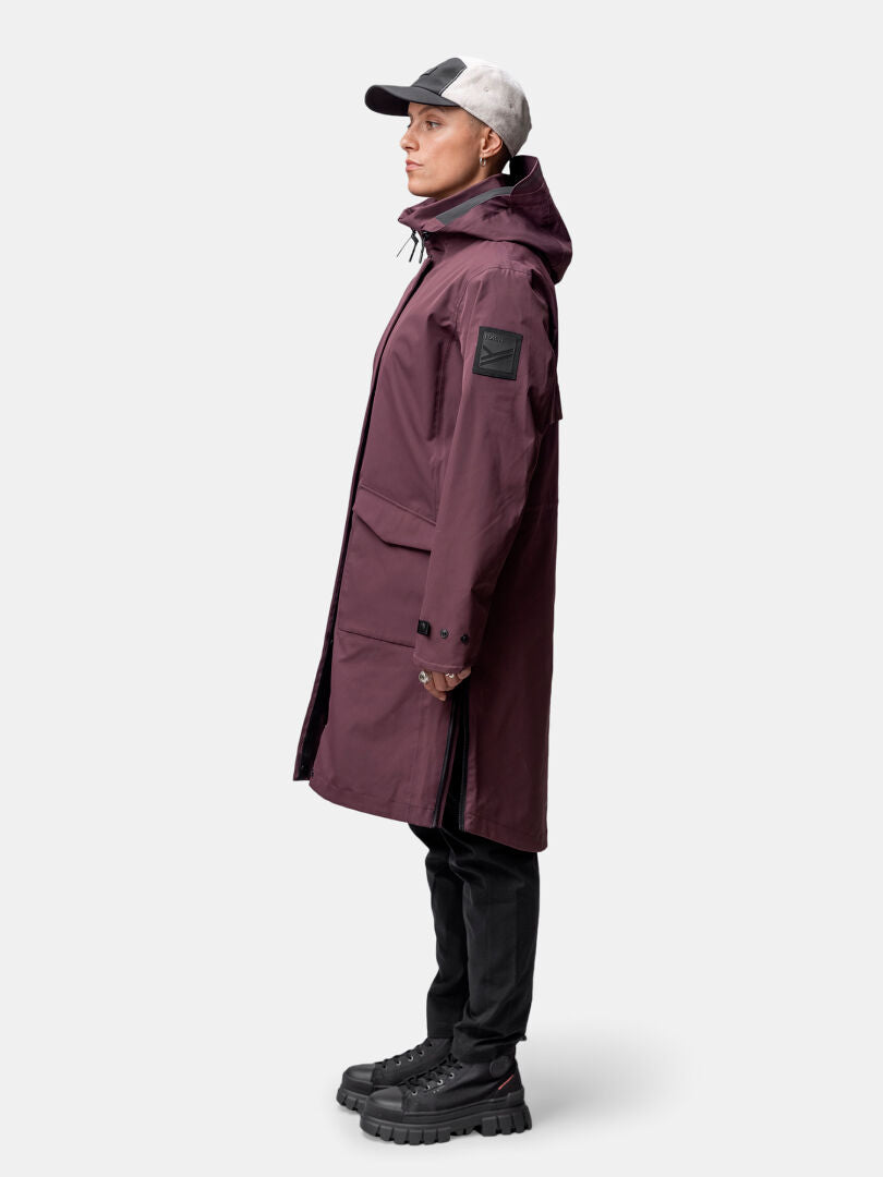 Person in a Halti Tokoi II DX Parka Jacket Womens (maroon), black pants, chunky shoes, and cap, side view.