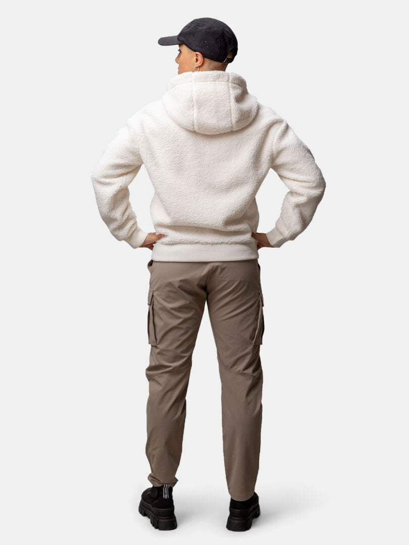Woman stands with hands on hips, wearing Halti Lykky Fleece Jacket in white, khaki cargo pants, black shoes, and a black cap.