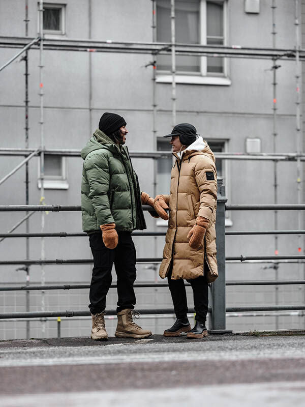 Two men in Halti Brahe Puffer Winter Jackets chat on a city street, bundled up warmly by a building with scaffolding.