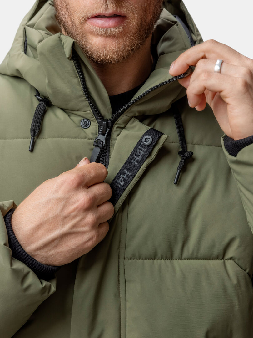 A person in a Brahe Puffer Winter Jacket by Halti zips up, showing a black HALO-tagged strip near the zipper.