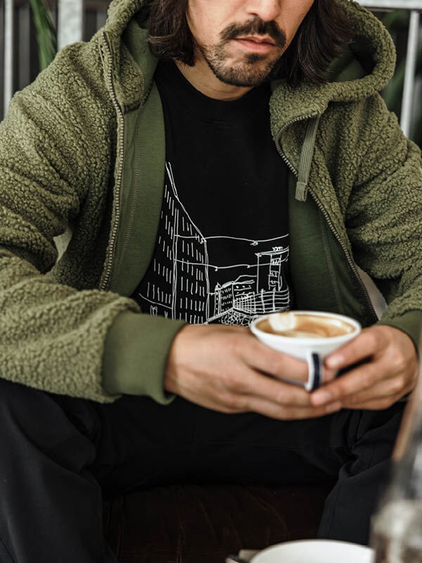 A man in a Halti Lykky Fleece Jacket holds a latte indoors.