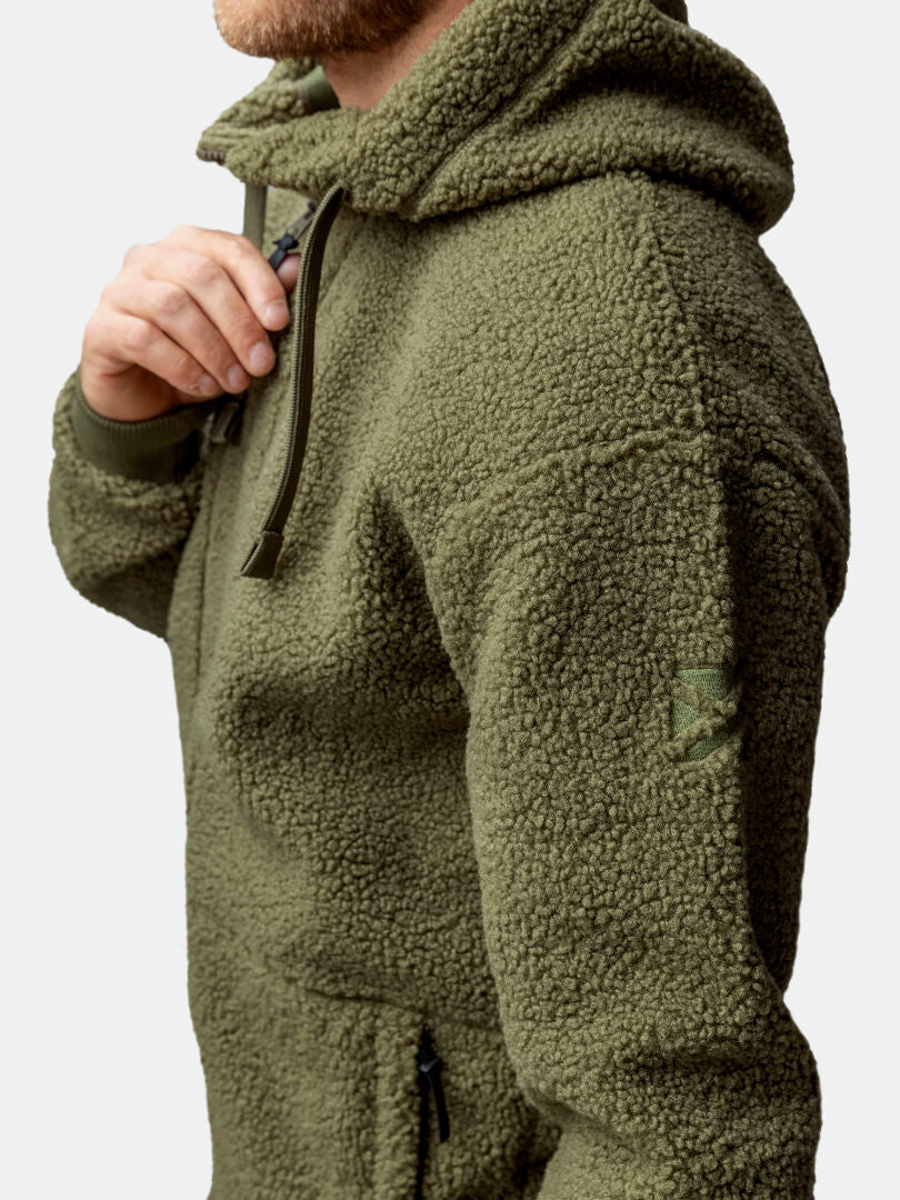 A person wears the Halti Lykky Fleece Jacket Men’s in olive green, featuring a zipper pocket and drawstring hood.