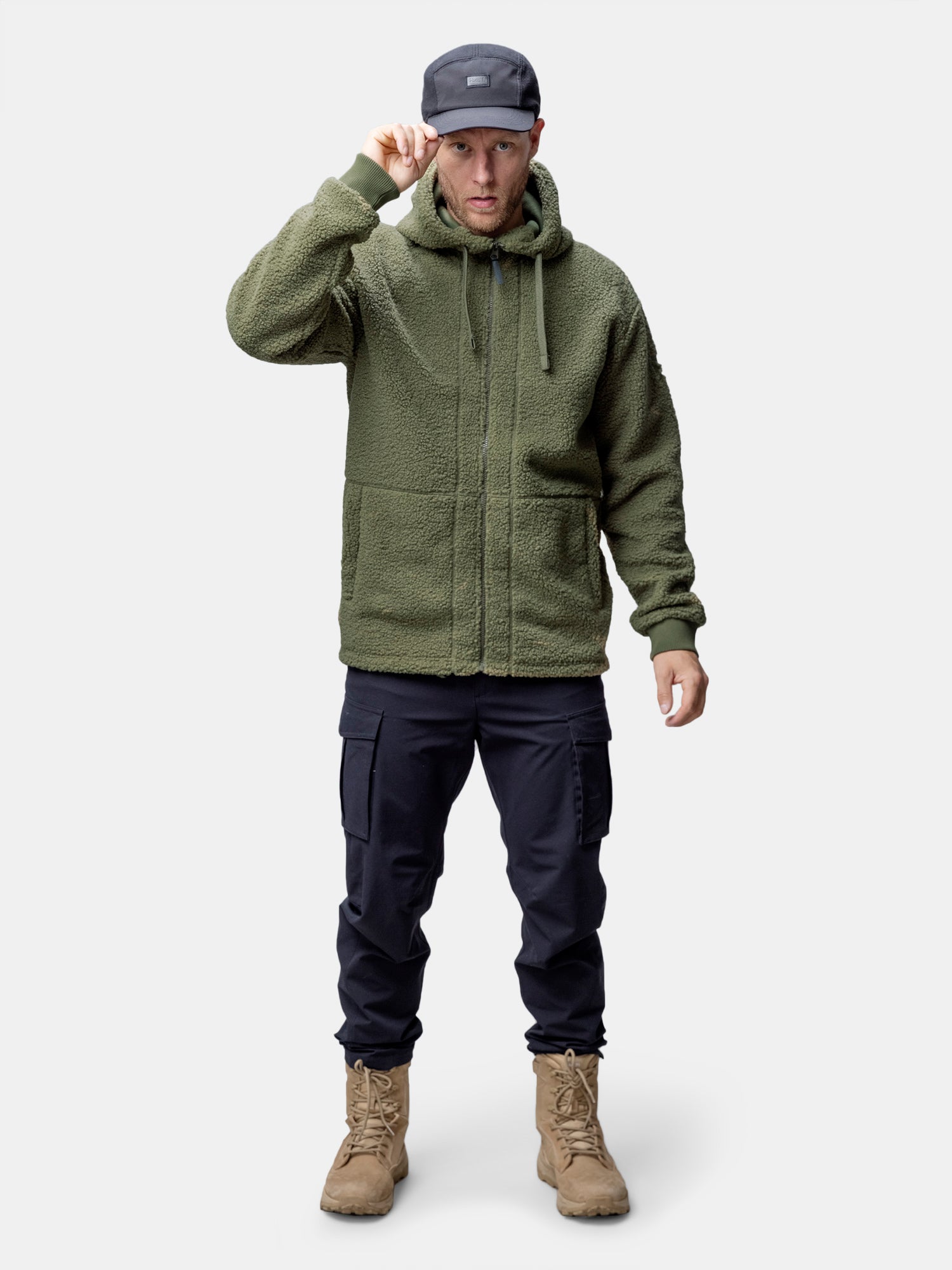 A man in a Halti Lykky Fleece Jacket, black cargo pants, tan boots, and a dark cap stands facing forward.