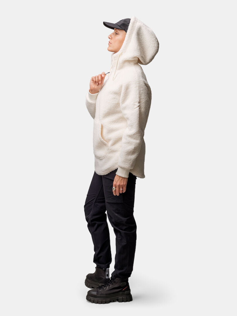 A woman in a Halti Lykky Fleece Pullover and black pants stands in profile against a plain background.