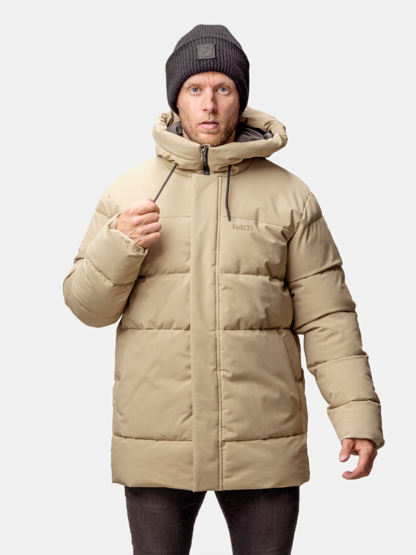 A man in a Halti Sammal Insulated Parka Jacket and a dark gray knit beanie stands against a light gray background.