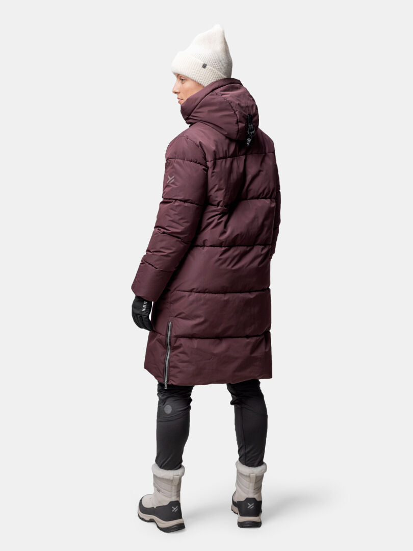 Person in a Halti Sammal Insulated Parka Jacket stands facing away, wearing a white beanie, gloves, and winter boots.