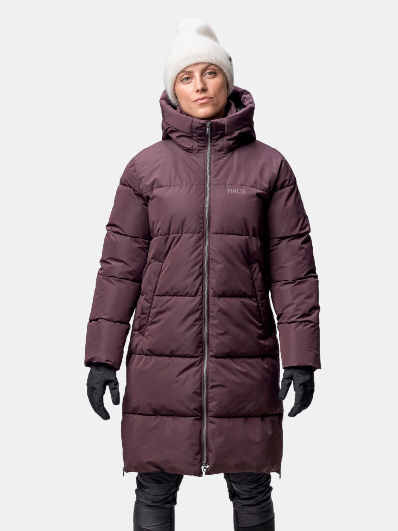 A woman wears the Halti Sammal Insulated Parka Jacket with DrymaxX®, a white beanie, and black gloves facing forward.