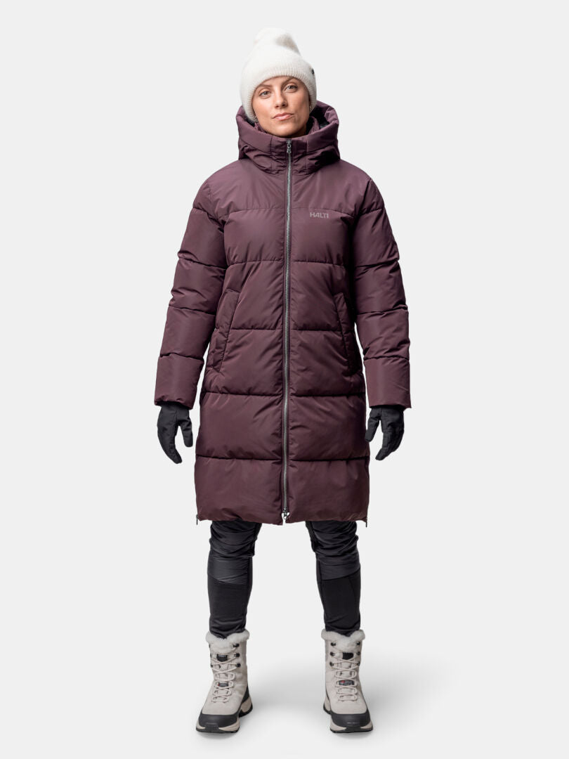 A person wears a Halti Sammal Insulated Parka Jacket for women, white beanie, black gloves, dark pants, and light boots.