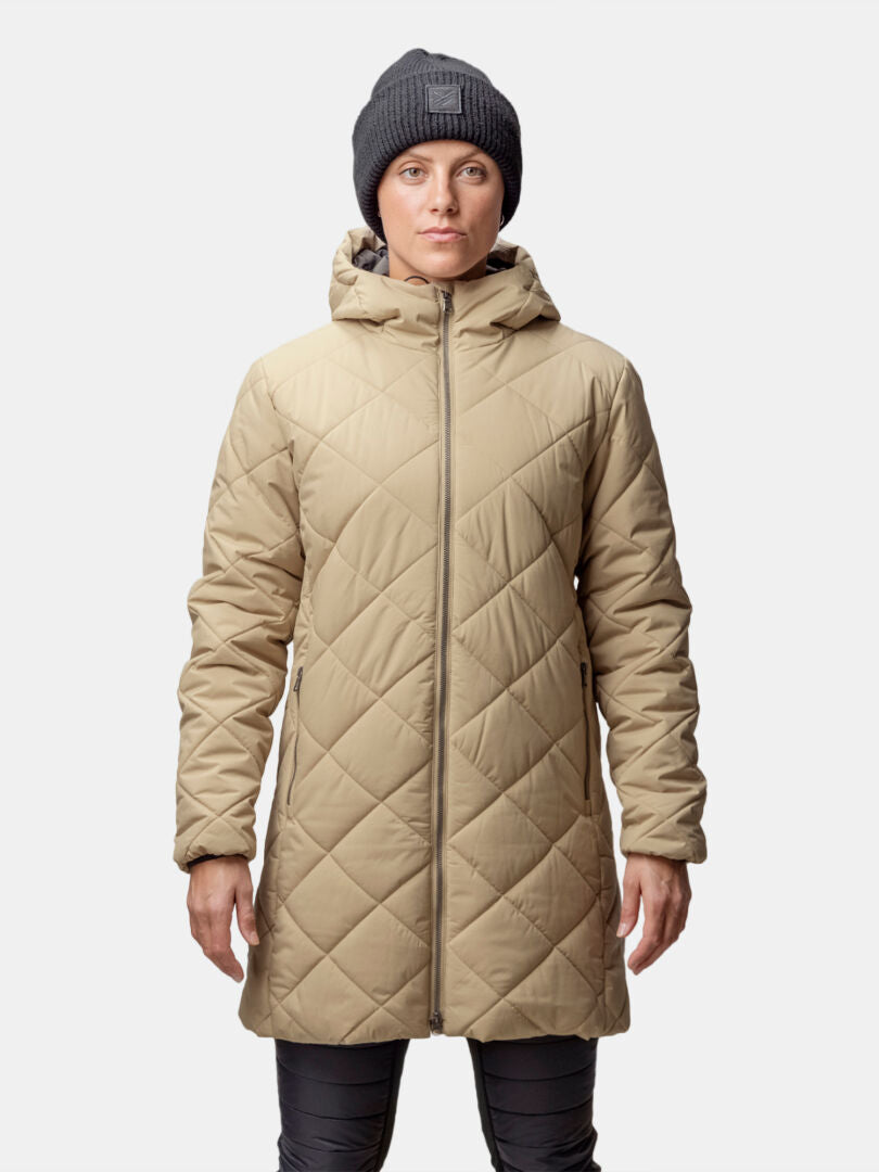 A woman wears the Halti Haapa Quilted Coat Jacket in beige, a gray beanie, and dark pants against a plain background.