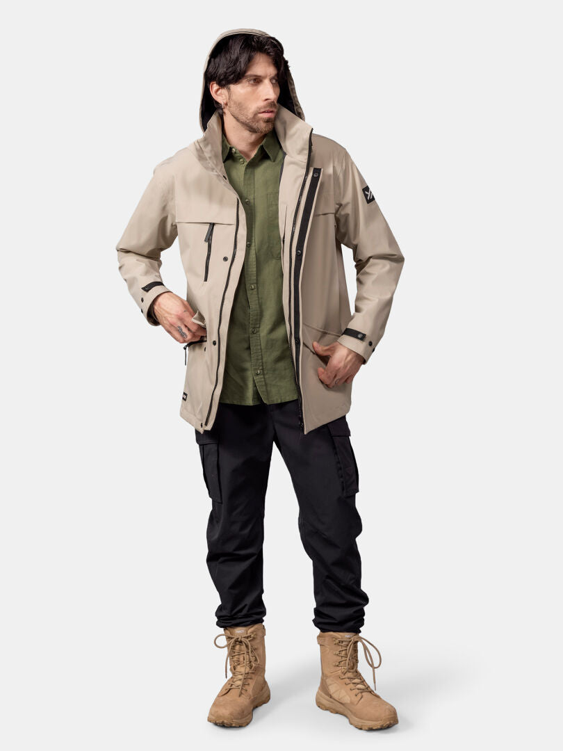A man wears the Halti Tokoi DX Jacket Men's, green shirt, black cargo pants, and tan boots against a plain background.