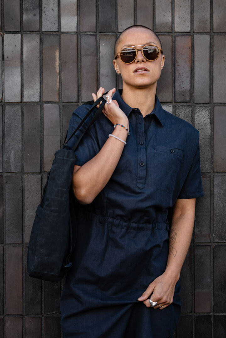 Person with short hair in sunglasses and a dark collared shirt holds the Halti Notsgi Dress Women's against a tiled wall.