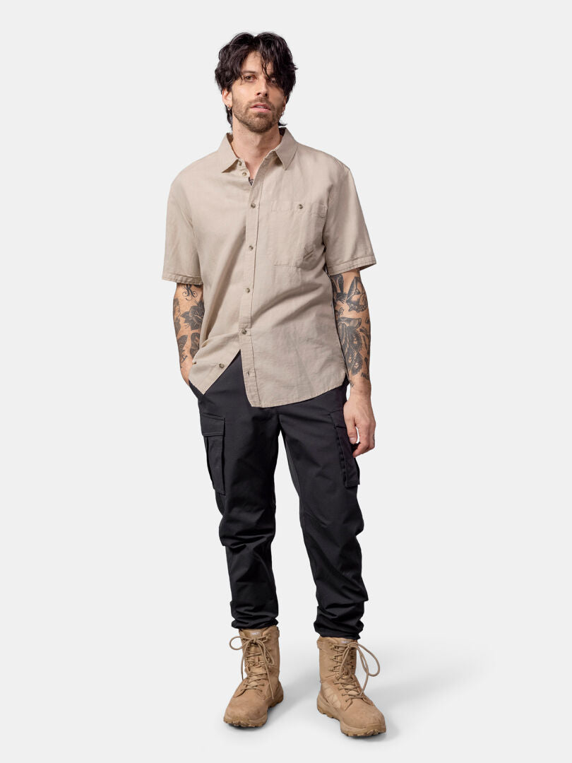 Man wearing Halti Notsgi Shirt Men's in beige, black cargo pants, and tan boots against a plain background.