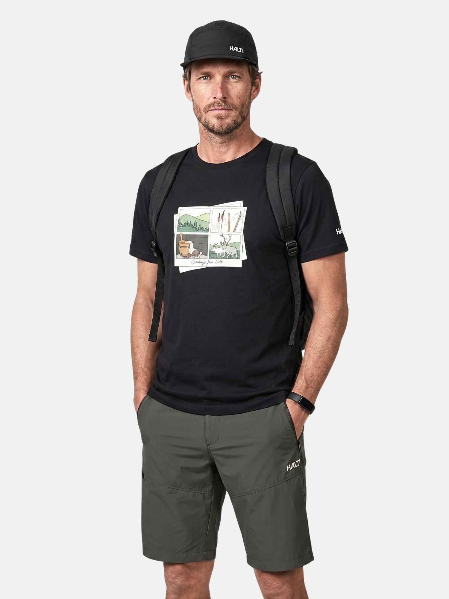 Man wearing Halti Matka II T-shirt, black cap, gray shorts, backpack, and smartwatch stands against a plain background.