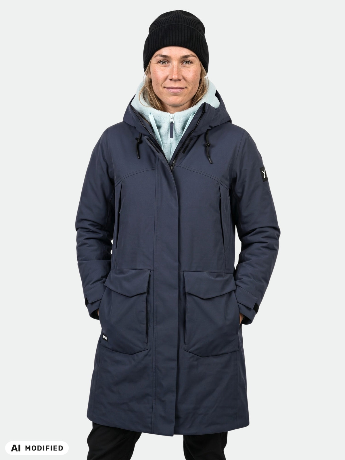 Person in Halti Kallio DX Parka, light hoodie, and black beanie stands against a plain light background.