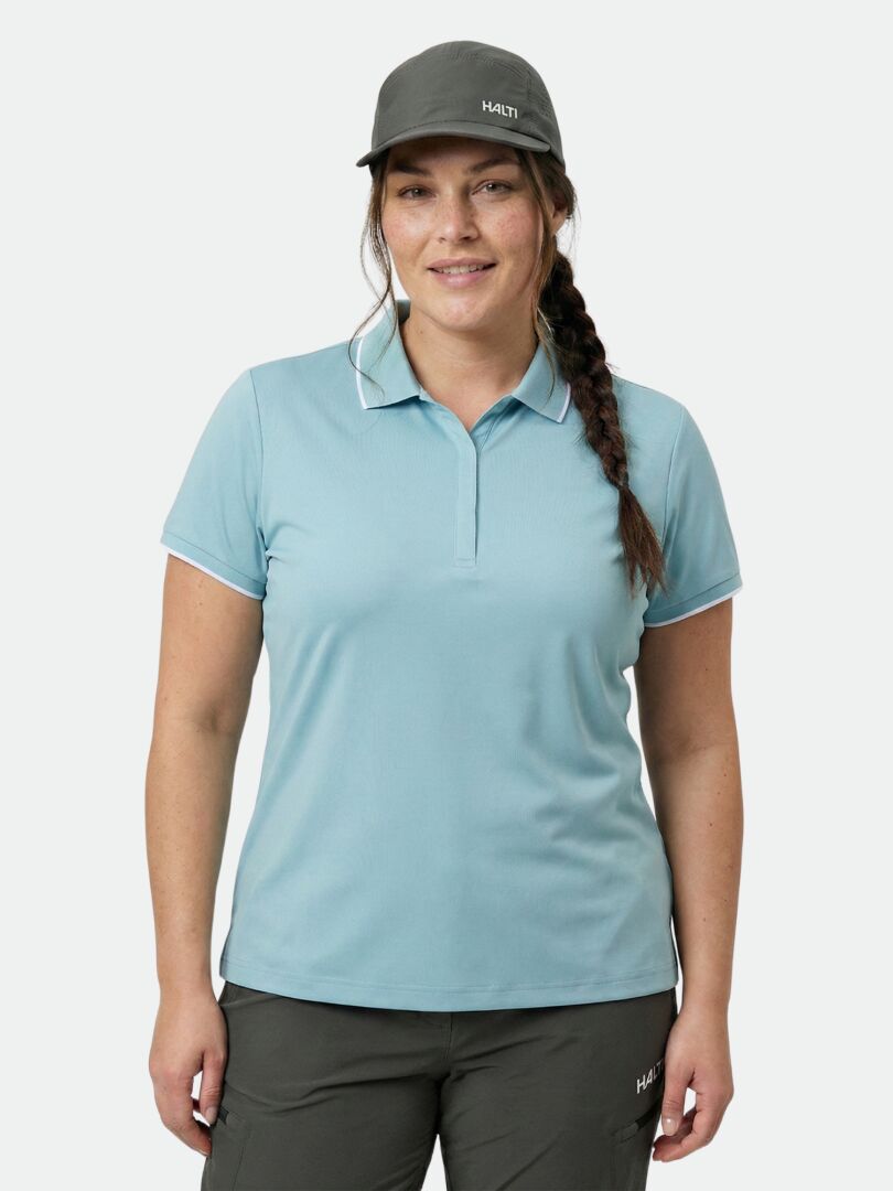 A woman wears the Halti Swingi Technical Polo Shirt Women's Plus in light blue and dark pants, facing the camera.