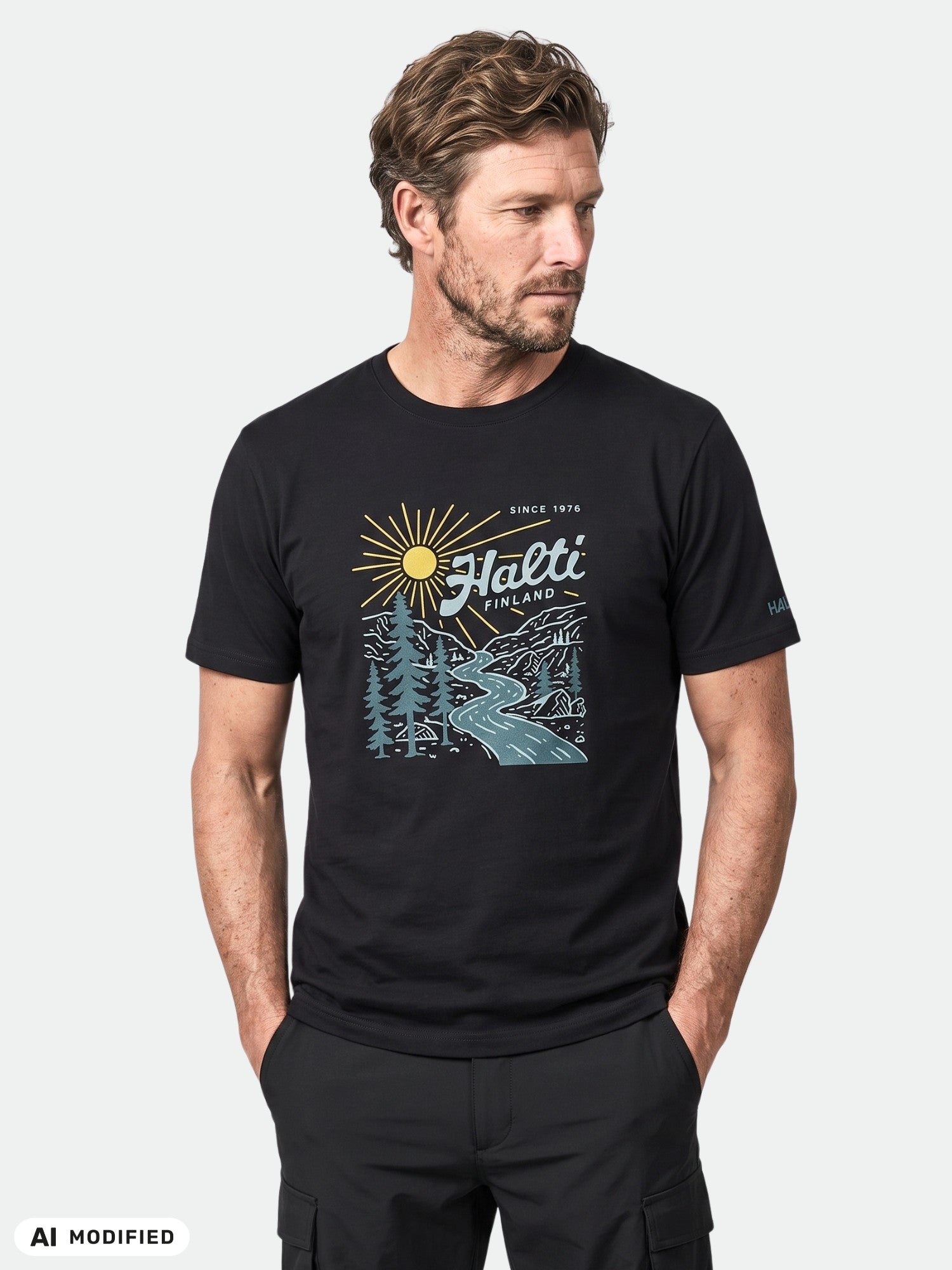 Man wears Halti Vehka unisex tee in black with sun, trees, river print and “Halti Finland” text, hands in pockets.
