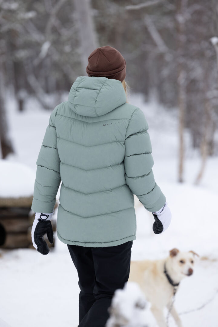 A person wearing Halti Routa Winter Pants Women's walks outside in the snow with a white dog.