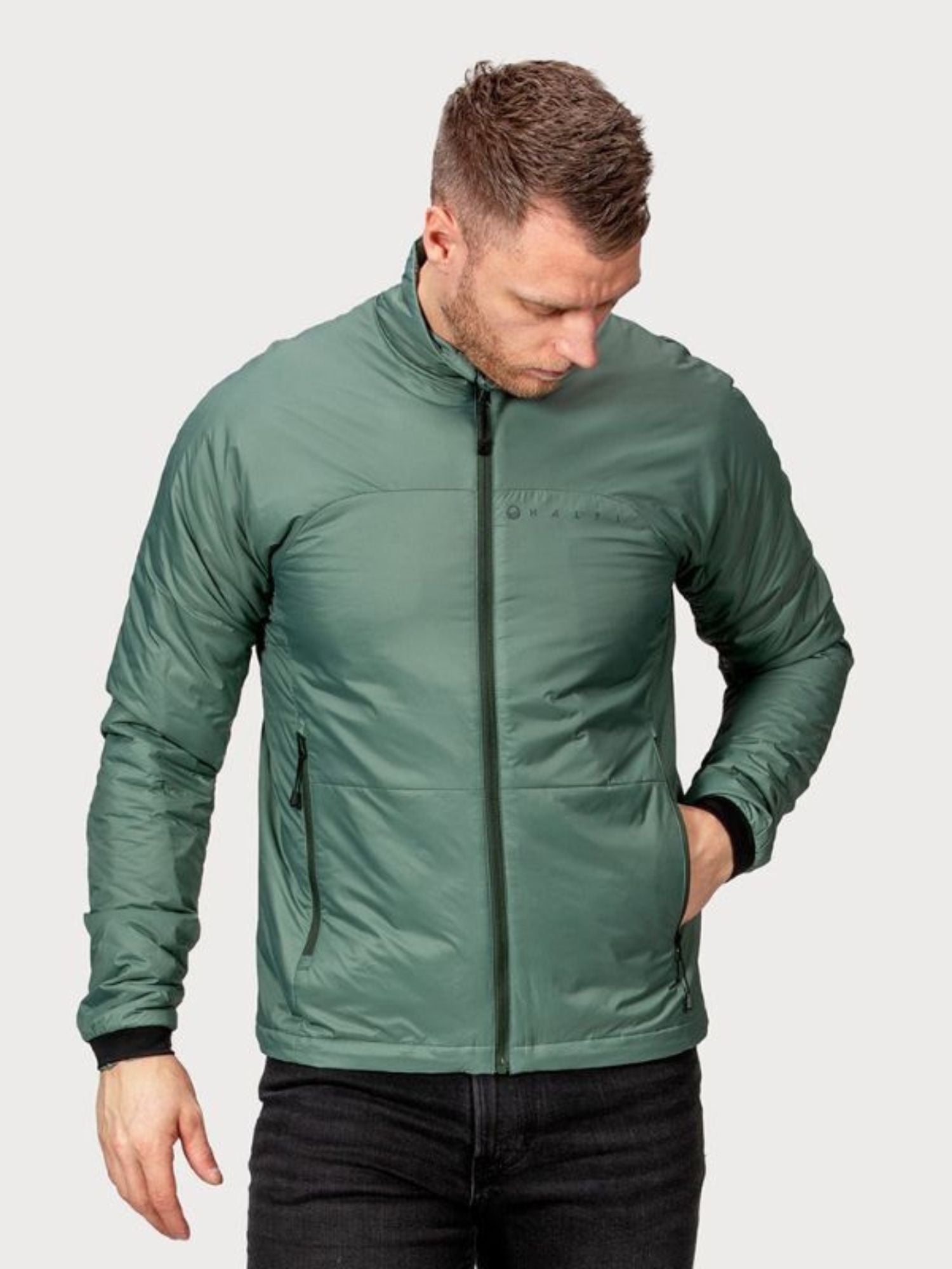 A man wears the Halti Neon Insulation Jacket Men's with PrimaLoft, hand in pocket, looking down against a plain background.