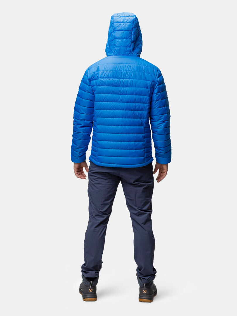 A person faces away wearing Halti’s Huippu Down Jacket Men’s in blue, with dark pants and black shoes.