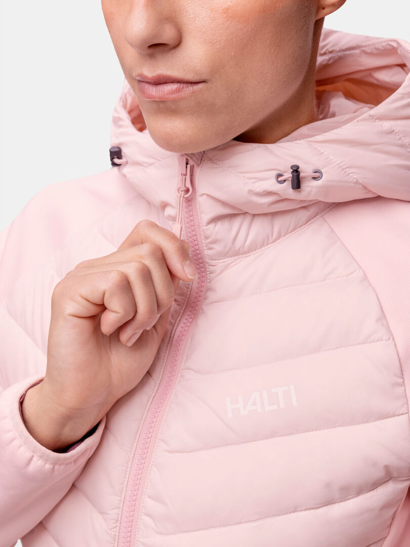 A woman zips up the Halti Huippu Hybrid Down Jacket with a hood, shown from the shoulders up.