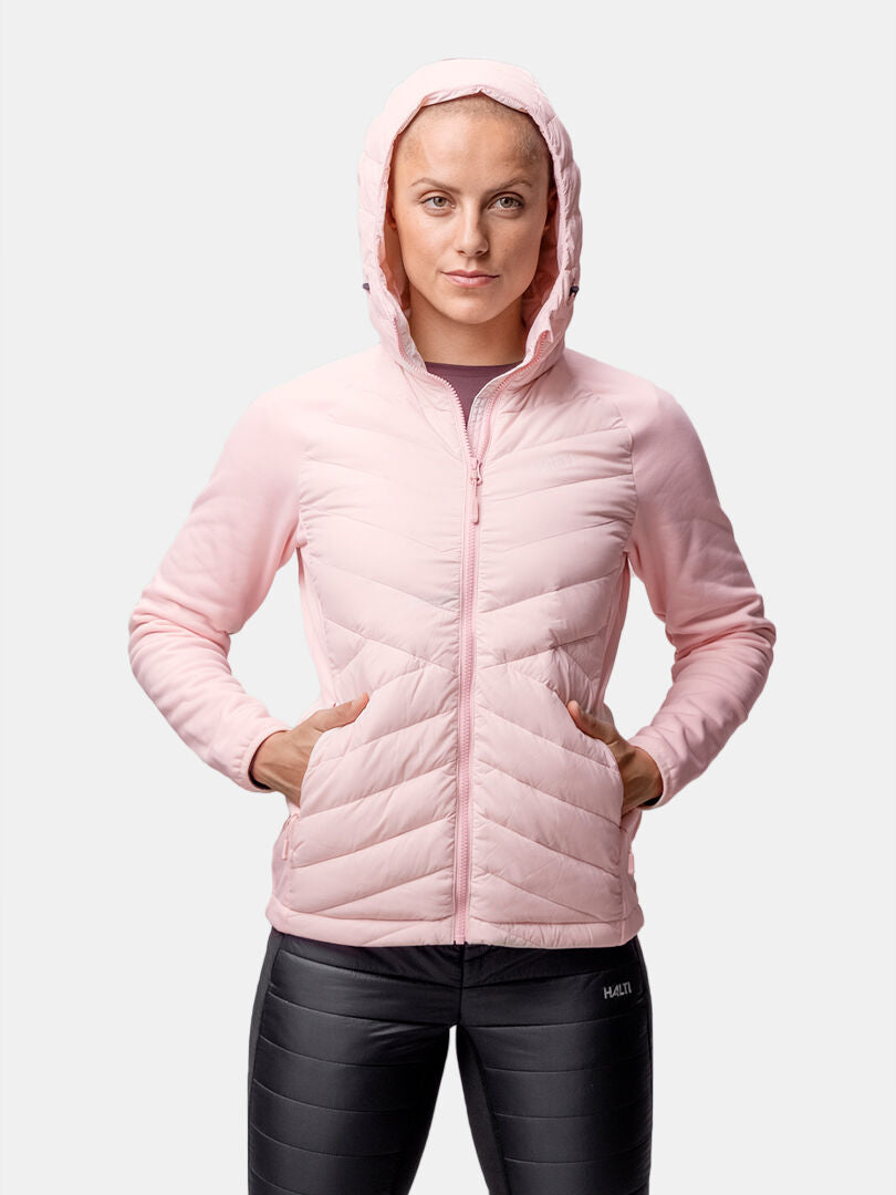 Woman in a light pink Halti Huippu Hybrid Down Jacket with Pertex Quantum ripstop, black leggings, hands in pockets.