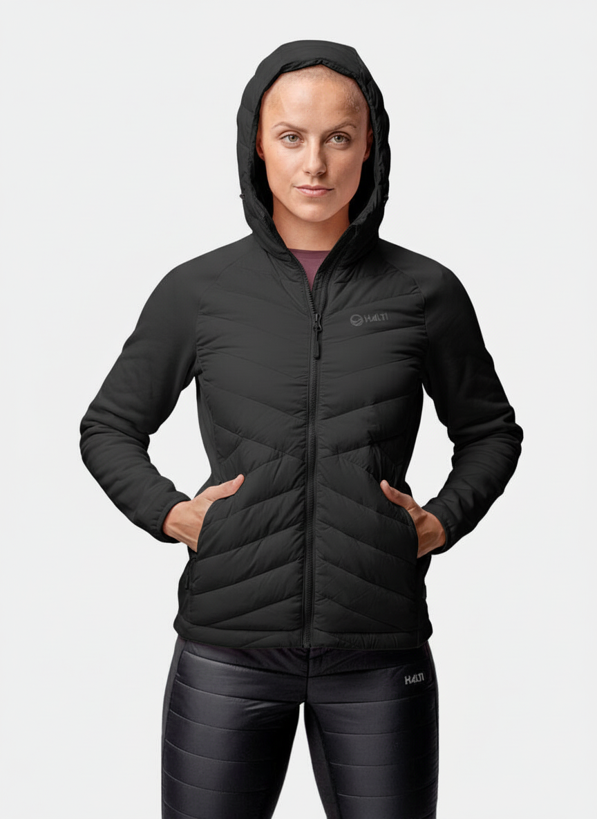 A woman wears the Halti Huippu Hybrid Down Jacket with leggings, hands in pockets, against a white background.