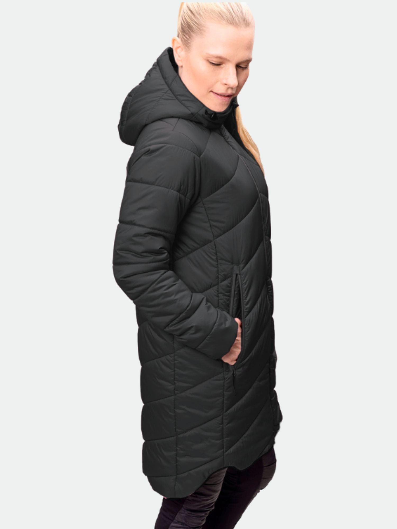 A woman in the Halti Komu Long Thermal Jacket, black, with hands in pockets, facing sideways.