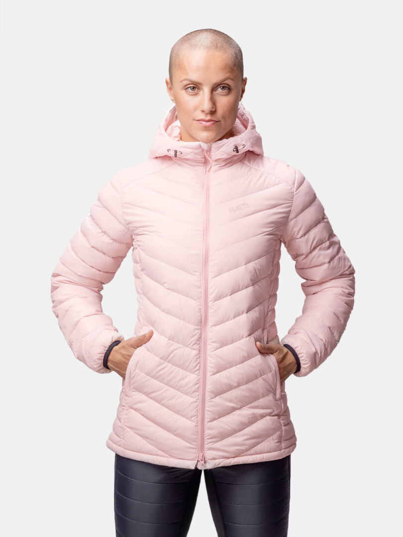 A person wears the Halti Huippu Mid Down Jacket Womens in light pink, facing forward with hands in pockets.