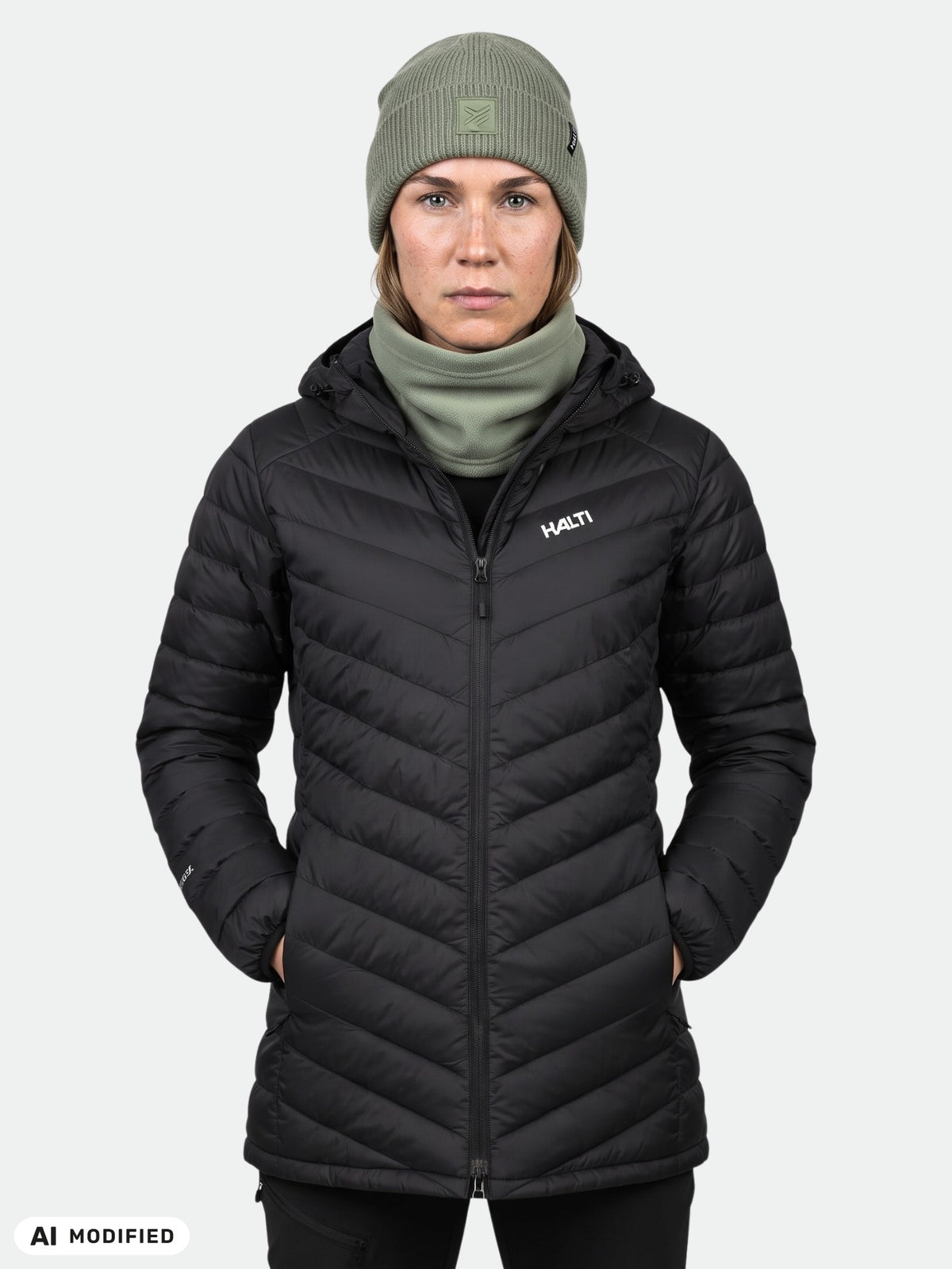 Woman in a black Halti Huippu Mid Down Jacket, green beanie, and neck gaiter against a plain light background.