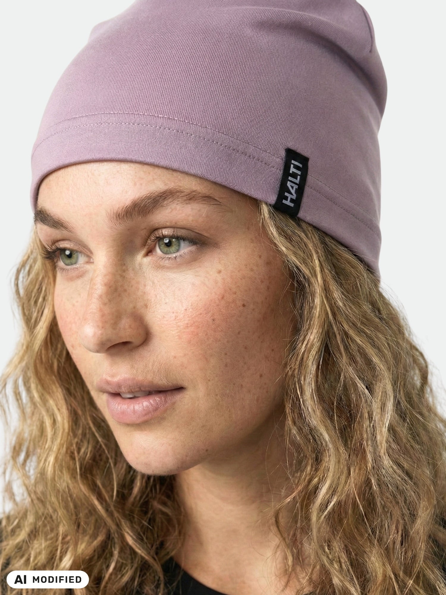 A person with curly hair wears a light purple Halti Loiva Beanie and glances slightly to the side.