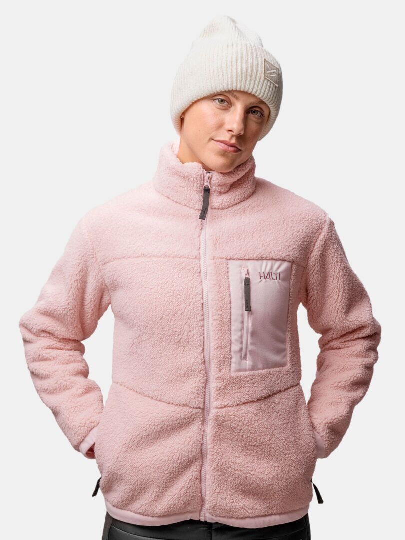 Person wears a light pink fleece jacket with a chest pocket and the Halti Huurre Beanie, hands in pockets.