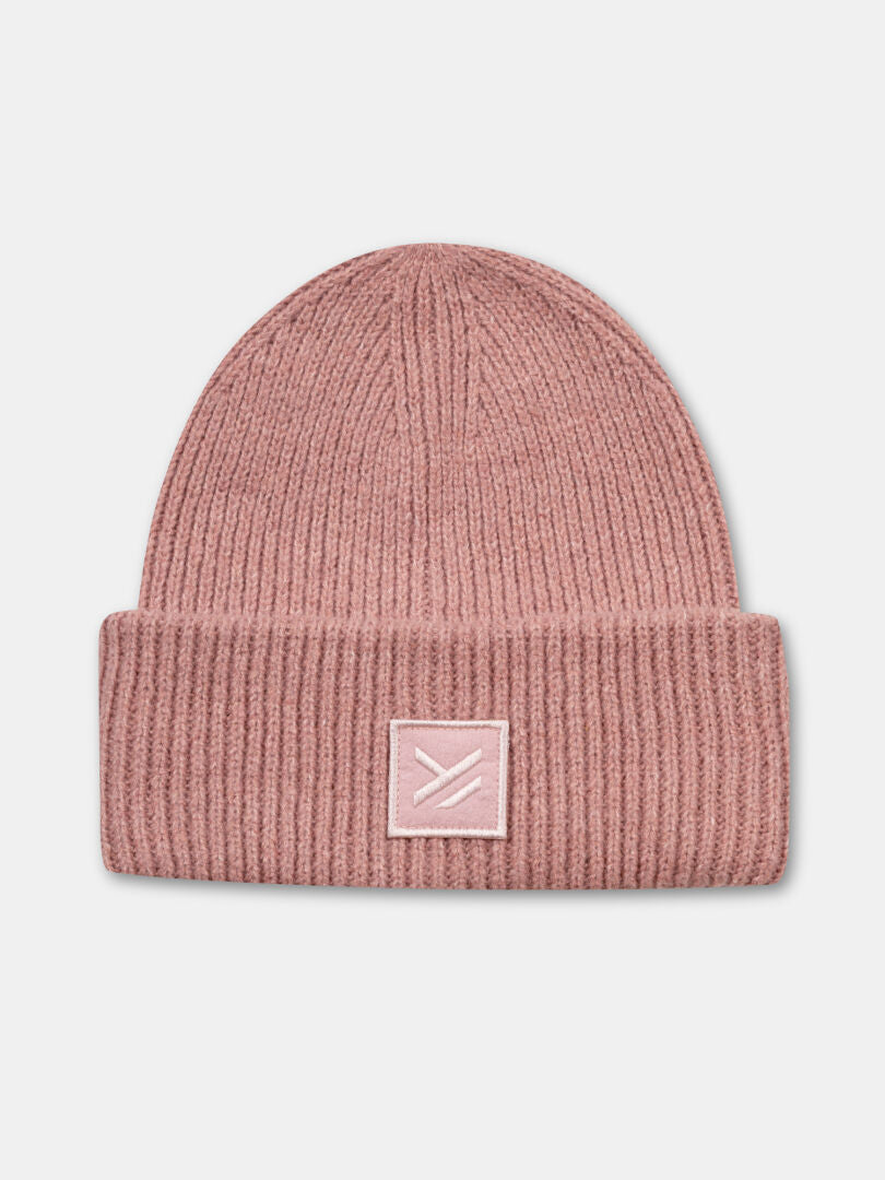 The Halti Huurre Beanie is a light pink, chunky rib knit hat with a folded brim and geometric patch.