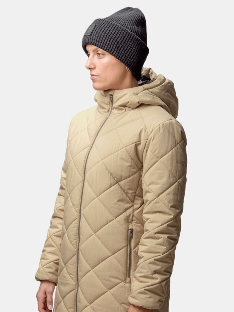 A person in a beige quilted hooded coat and Halti Huurre Beanie stands against a plain background.
