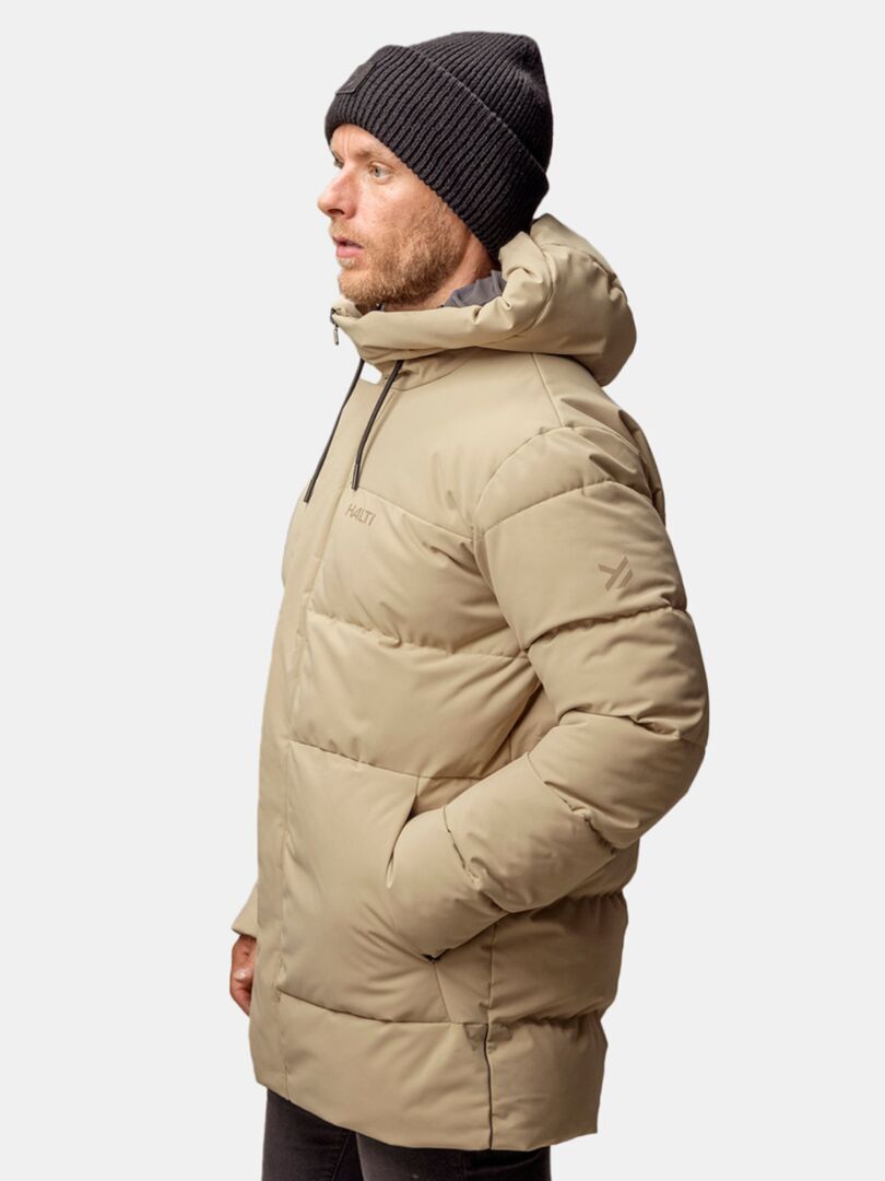 A man in a beige puffer jacket and Halti Huurre Beanie stands facing left against a white background.