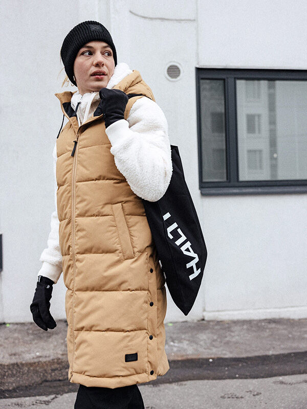 Person wearing Halti Huurre Headband, tan puffer vest, and white hoodie walks outside with a black bag.